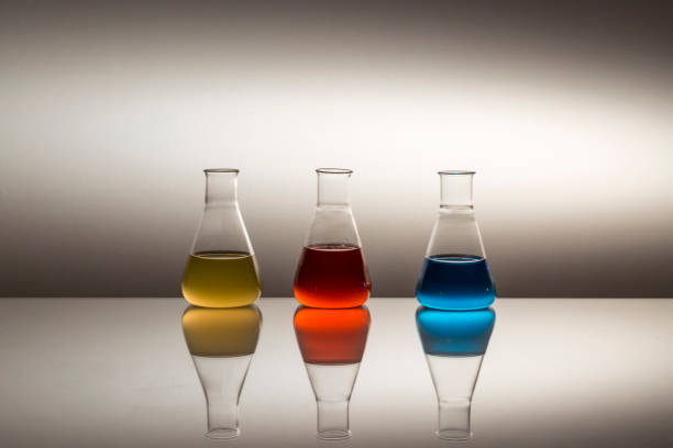 istock Scientific laboratory glass erlenmeyer flask filled with yellow, red and blue liquid on reflective surface. 1205245444