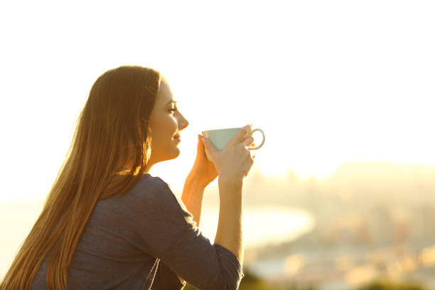 コーヒーマグカップを持つ夕日を考えている女性 - バルコニー ストックフォトと画像