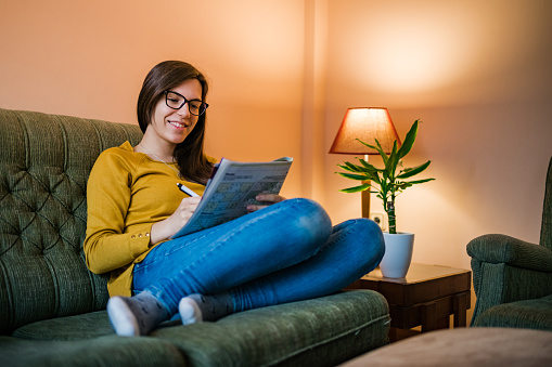 Young woman enjoying leisure time at home solving sudoku puzzles or crosswords.