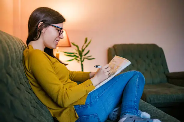 Young woman enjoying leisure time at home solving sudoku puzzles or crosswords.