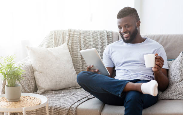 cheerful black man reading news on digital tablet with coffee - mobility working digital tablet people imagens e fotografias de stock