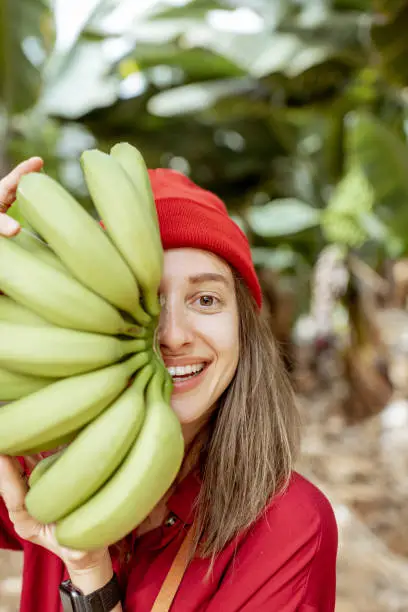 Facial portrait of a cute woman holding a stem with fresh green bananas in front of her face. Healthy eating and wellness concept