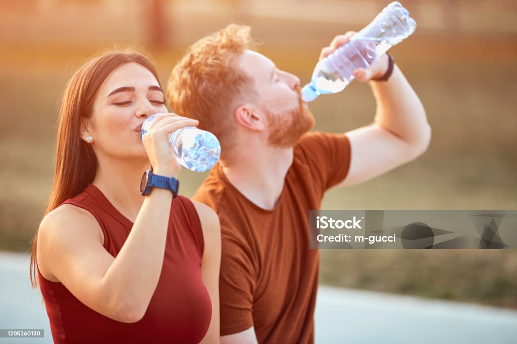 Modern couple making pause in an urban park during jogging / exercise. Drinking Stock Photo