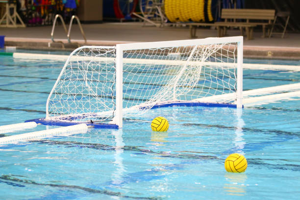 Two yellow water polo balls floating on the water near the goal net Indoor photo of two yellow water polo balls floating on the water near the goal net. water polo stock pictures, royalty-free photos & images