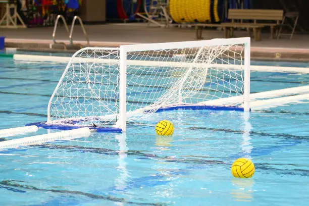 Indoor photo of two yellow water polo balls floating on the water near the goal net.