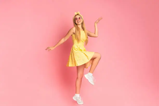 Photo of Cheerful woman dancing jumping over pink studio wall