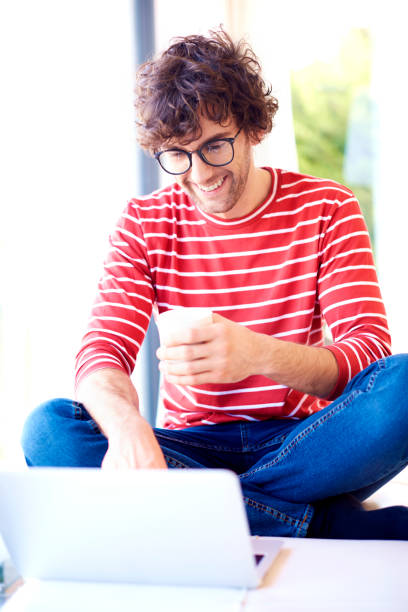 istock Smiling man with eyeglasses using his laptop and drinking tea at home 1205264787