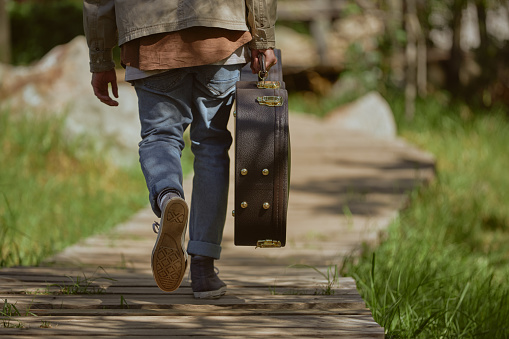 Cropped shot of an unrecognizable man walking and carrying his guitar case during a day out in the forest alone