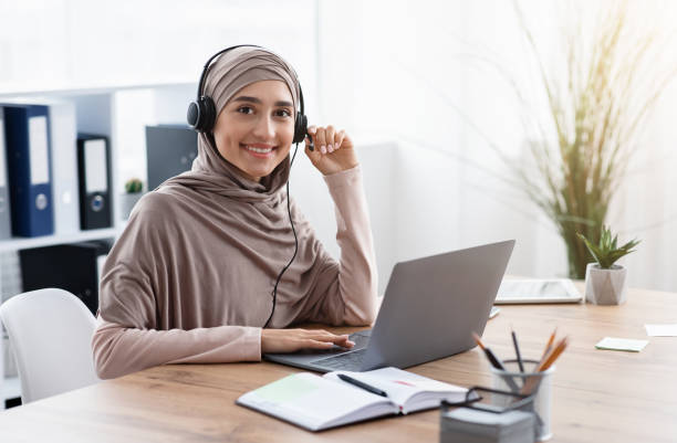 funcionária árabe em fone de ouvido assistindo webinar em laptop no escritório - traditional clothing audio - fotografias e filmes do acervo