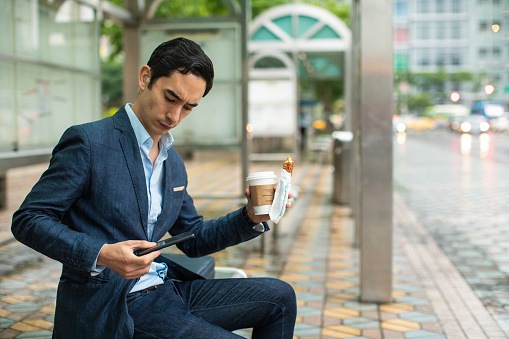 Modern businessman using smartphone on bus stop