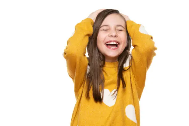 Photo of Waist up studio portrait of an adorable young girl laughing with excitement, head in hands and closed eyes, isolated on white backgroud. Human emotions and facial expressions concept.
