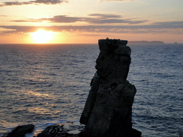 istock High rock formation emerges from the sea at sunset with clouds 1205270012