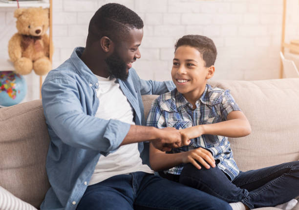 istock Father And Son Bumping Fists Sitting On Couch At Home 1205272287