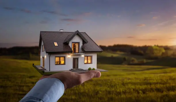 Photo of Male hand showing, offering a new dream house at the empty field with copy space