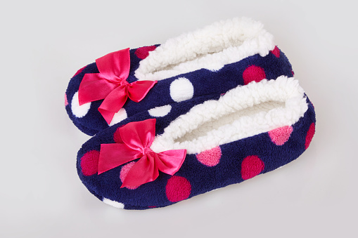 A pair of colorful polka dot patterned warm cozy slippers with pink satin bows on a white background.
