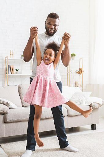 Emotional african father lifting up his cute happy little daughter, having fun together at home