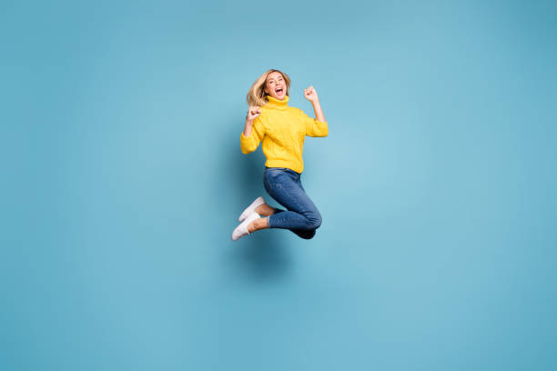 foto de perfil completo de senhora louca pulando alto celebrando viagem livre vencedora ao exterior regozijando usar jeans amarelo de malha - jump for joy - fotografias e filmes do acervo