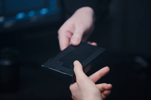 Hacker offers his partner to take a black mystery box. Close-up of hands on a background of monitor.