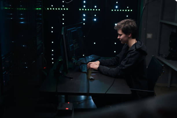 istock Joyful female hacker in a dark hoodie and in a dark room hacking a computer network 1205286083