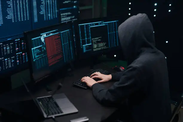 Photo of Computer hacker coding on keyboard on a background of monitors.