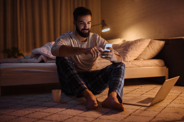 homme barbu bel utilisant le téléphone dans la chambre à coucher la nuit - carpet caucasian domestic room home interior photos et images de collection