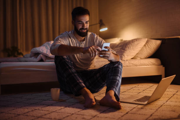 Handsome bearded man using phone in bedroom at night