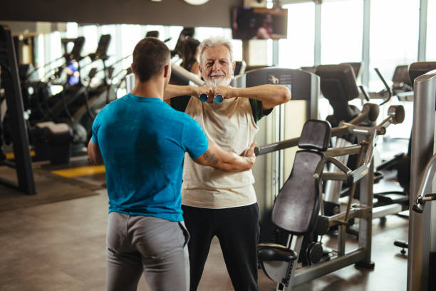 istock Senior man exercising with personal trainer using dumbbells at the gym 1205290983
