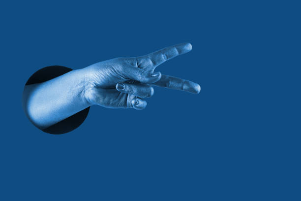 Hand shows  different gestures and symbols from the hole on a blue paper background. Template for design. Trend color of 2020 concept. The color of the year. Classic deep blue.
