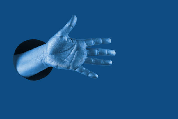 istock Hand shows  different gestures and symbols from the hole on a blue paper background. Template for design. Trend color of 2020 concept. 1205291611