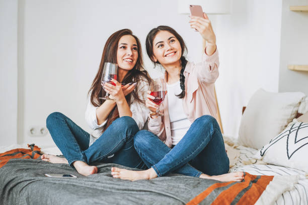 joven despreocupada morena chicas amigos en casual con copas de vino tomando selfie y divirtiéndose juntos en la fiesta en casa - drinking little girls women wine fotografías e imágenes de stock