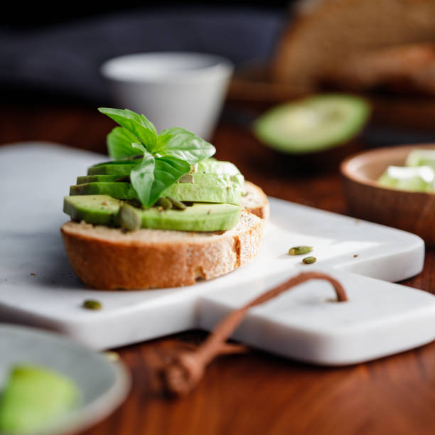 istock Avocado toast with pepitas and fresh basil on a white marble cutting board. Home cooking, healthy eating concept. 1205298845