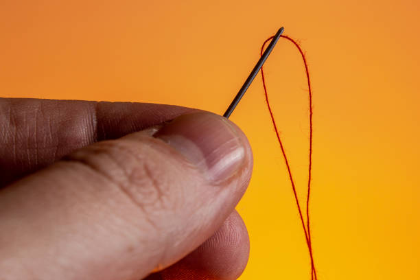 istock needle in hand with a red thread on a Lush Lava background. close up copy space 1205301046