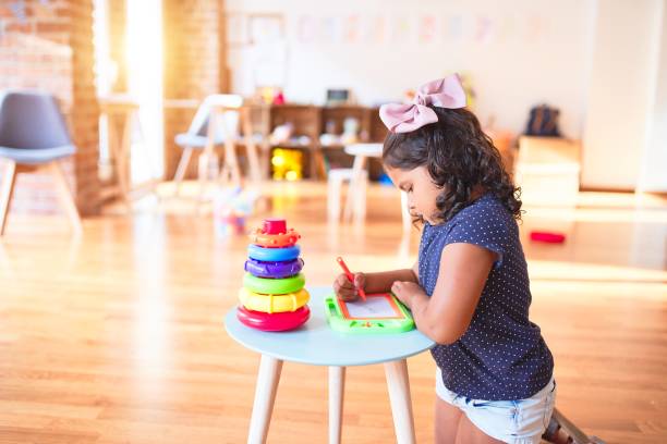 istock Beautiful toddler girl drawing cute draw using digital board at kindergarten 1205301859