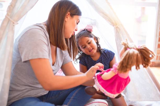 beautiful teacher and toddler girl sitting on the floor playing with unicorn and doll inside tipi at kindergarten - preschooler child playing latin american and hispanic ethnicity imagens e fotografias de stock