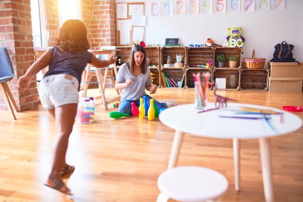 beautiful teacher and toddler girl playing bowling at kindergarten - preschooler child playing latin american and hispanic ethnicity imagens e fotografias de stock