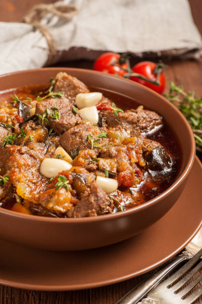 istock Braised meat with vegetables in a thick sauce. A large portion in a deep plate is ready to eat. Rustic decoration on a dark wooden background. 1205303628