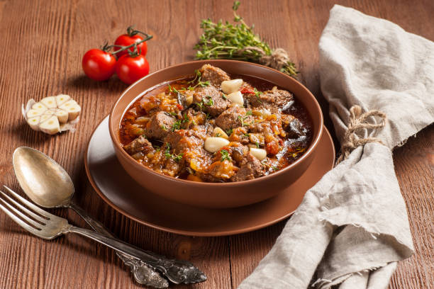 istock Braised meat with vegetables in a thick sauce. A large portion in a deep plate is ready to eat. Rustic decoration on a dark wooden background. 1205303641