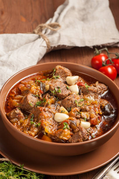 istock Braised meat with vegetables in a thick sauce. A large portion in a deep plate is ready to eat. Rustic decoration on a dark wooden background. 1205303751