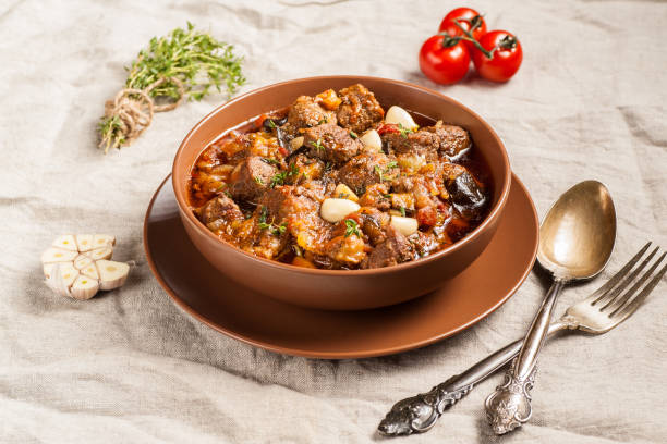 istock Braised meat with vegetables in a thick sauce. A large portion in a deep plate is ready to eat. Rustic decoration on a dark wooden background. 1205303768