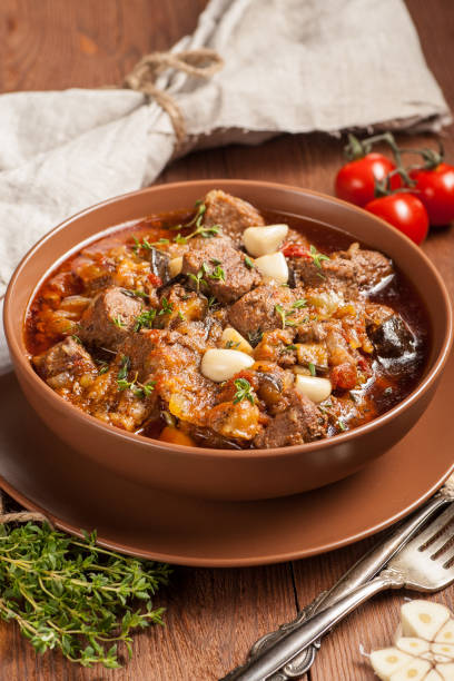 istock Braised meat with vegetables in a thick sauce. A large portion in a deep plate is ready to eat. Rustic decoration on a dark wooden background. 1205303795