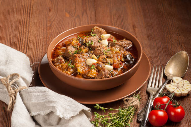 istock Braised meat with vegetables in a thick sauce. A large portion in a deep plate is ready to eat. Rustic decoration on a dark wooden background. 1205303834