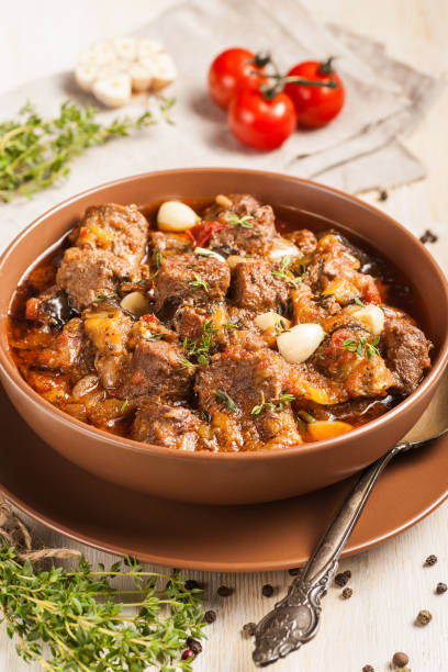 istock Braised meat with vegetables in a thick sauce. A large portion in a deep plate is ready to eat. Rustic decoration on a dark wooden background. 1205303846