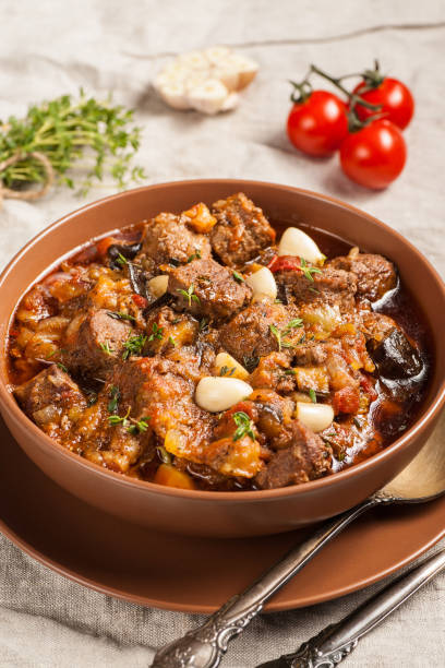 istock Braised meat with vegetables in a thick sauce. A large portion in a deep plate is ready to eat. Rustic decoration on a dark wooden background. 1205303943
