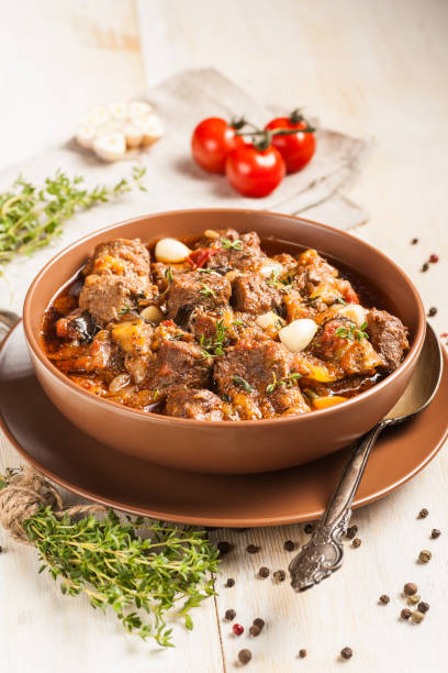 istock Braised meat with vegetables in a thick sauce. A large portion in a deep plate is ready to eat. Rustic decoration on a dark wooden background. 1205303965