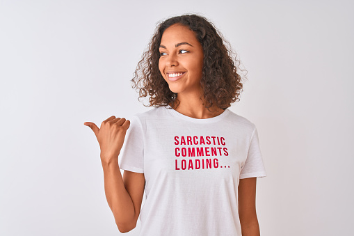 Brazilian woman wearing fanny t-shirt with irony comments over isolated white background pointing and showing with thumb up to the side with happy face smiling