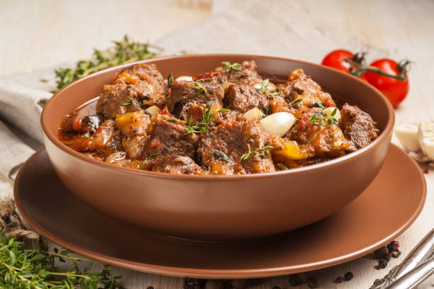 istock Braised meat with vegetables in a thick sauce. A large portion in a deep plate is ready to eat. Rustic decoration on a dark wooden background. 1205304214