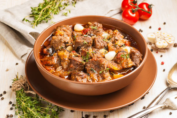 istock Braised meat with vegetables in a thick sauce. A large portion in a deep plate is ready to eat. Rustic decoration on a dark wooden background. 1205304216
