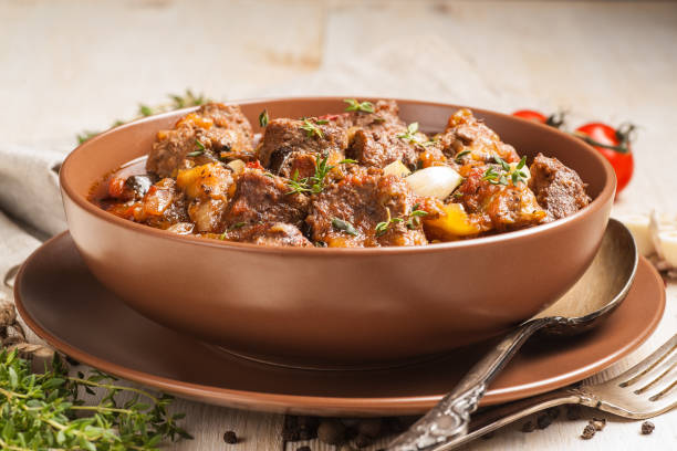 istock Braised meat with vegetables in a thick sauce. A large portion in a deep plate is ready to eat. Rustic decoration on a dark wooden background. 1205304286
