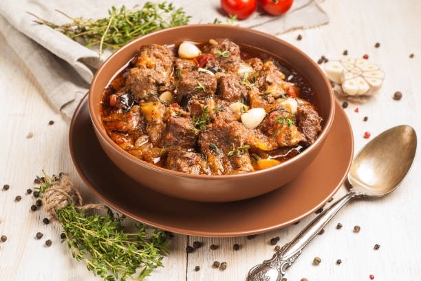 Braised meat with vegetables in a thick sauce. A large portion in a deep plate is ready to eat. Rustic decoration on a dark wooden background.