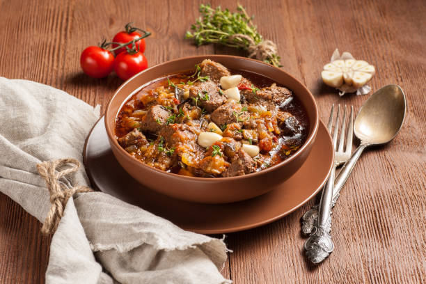 istock Braised meat with vegetables in a thick sauce. A large portion in a deep plate is ready to eat. Rustic decoration on a dark wooden background. 1205304379